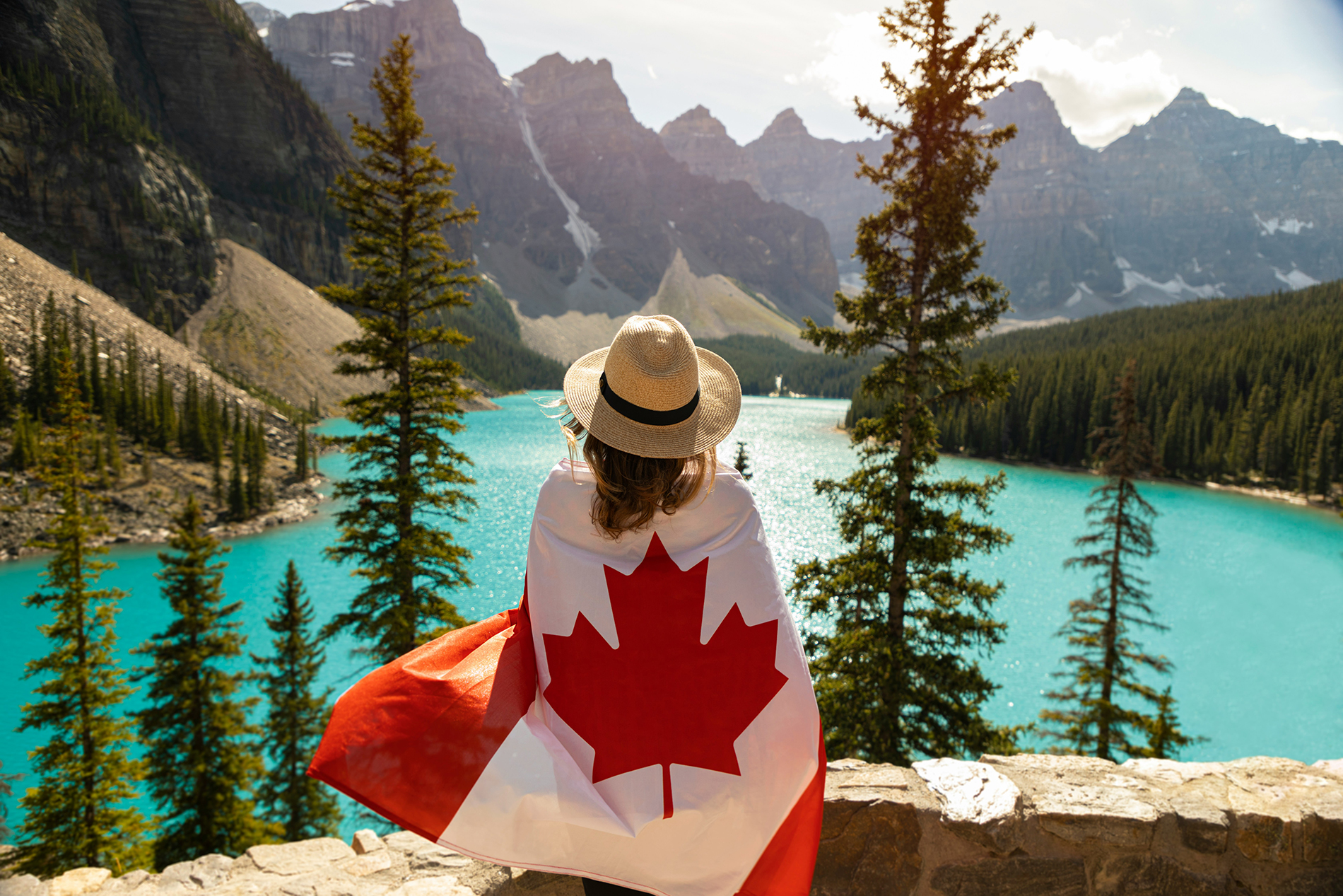 Touriste de dos enveloppée dans un drapeau canadien, admirant le lac Moraine dans les Rocheuses — image inspirante pour bien préparer son voyage au Canada.